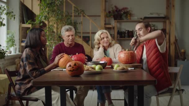 Junger Mann zeigt seinen Großeltern und einer Afroamerikanerin, wie man einen Kürbis für Halloween schneidet — Stockvideo