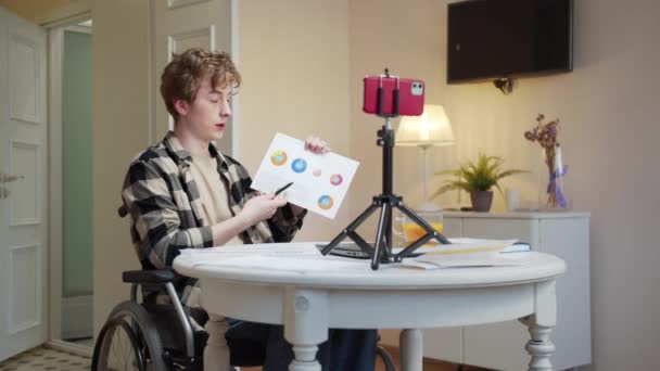 Un jeune homme handicapé parle avec quelqu'un et montre des diagrammes — Video