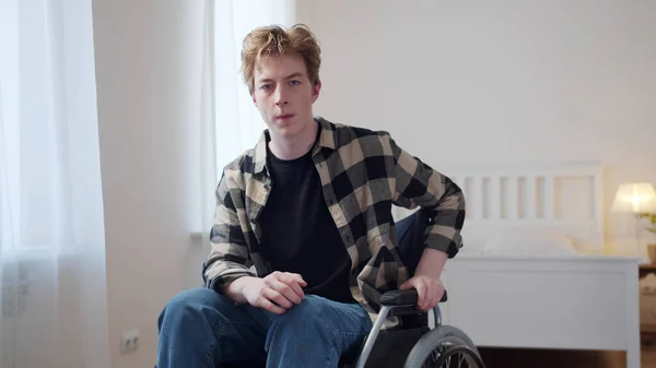 Молодой человек сидит в инвалидном кресле и серьезно смотрит в камеру — стоковое фото