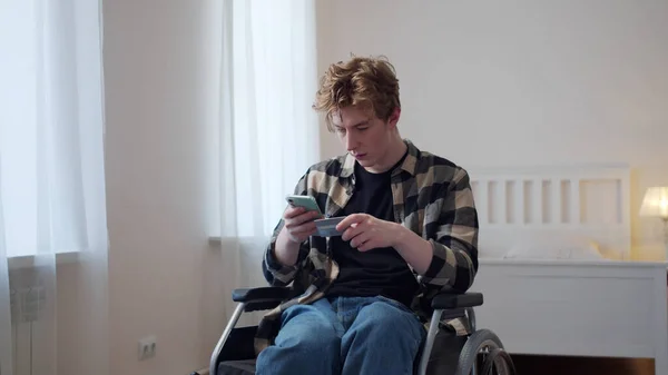 A disabled young man dials a number from a bank card — Stock Photo, Image