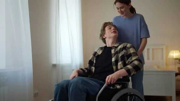 Uma jovem mulher está dirigindo seu amigo em uma cadeira de rodas — Fotografia de Stock