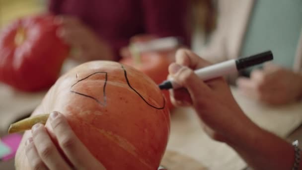 Un hombre usa un marcador para dibujar una boca en una calabaza — Vídeo de stock