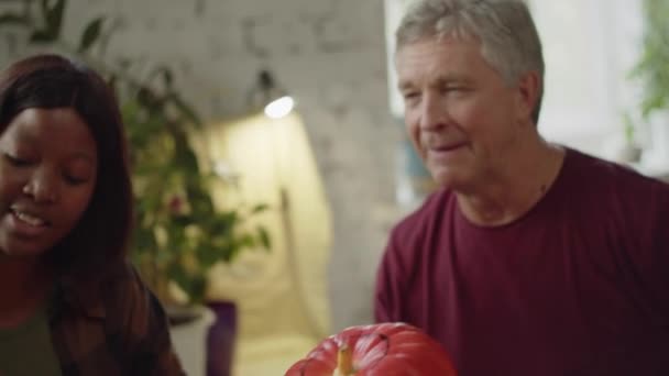 Black woman and old man sitting together at the table and drawing on a pumpkin — Stock Video