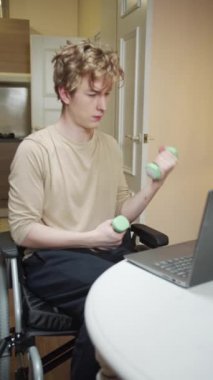 Genç engelli bir adam dambıllarla egzersiz yapıyor.