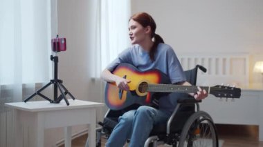 Engelli bir kadın gitar çalıyor ve şarkı söylüyor.