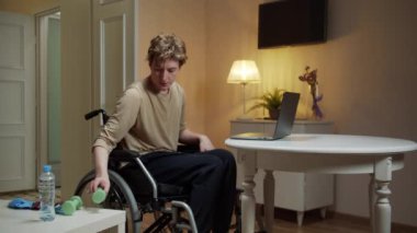 Genç engelli bir adam dambıllarla egzersiz yapıyor.