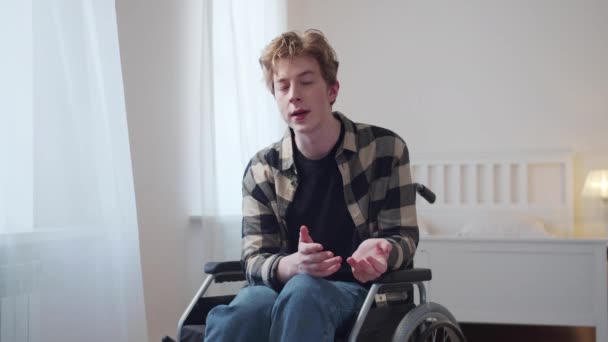 A young man is sitting in a wheelchair and talking to the camera — Stock Video