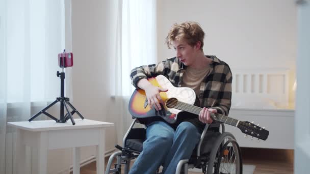 Een gehandicapte man maakt een video op een telefoon en speelt gitaar — Stockvideo