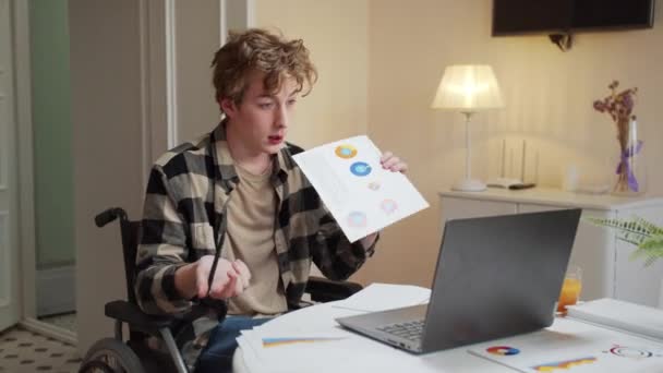 Инвалид молодой человек разговаривает с кем-то и показывает диаграммы — стоковое видео