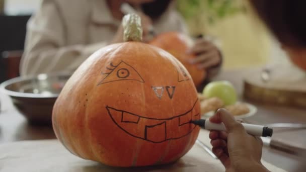Een volwassen dame is bijna klaar om een krik gezicht te tekenen op een halloween pompoen — Stockvideo