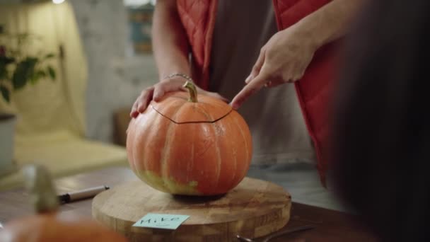 Seorang pria dalam rompi merah memotong bagian atas labu halloween — Stok Video