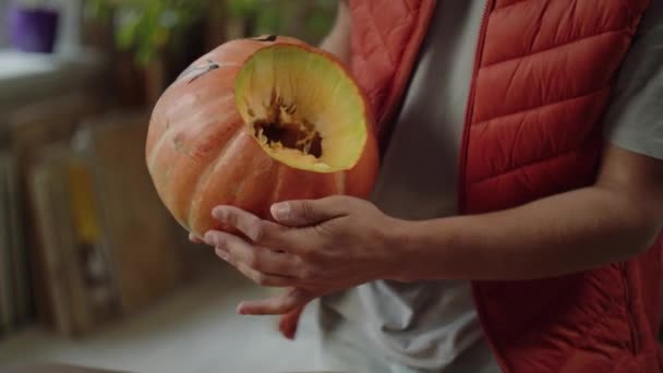 Un giovane in gilet rosso sta trasformando una zucca di Halloween — Video Stock