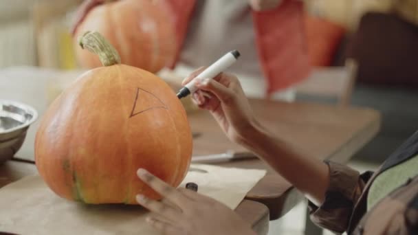 Uma jovem senhora está desenhando olhos e uma boca em uma abóbora de Halloween — Vídeo de Stock