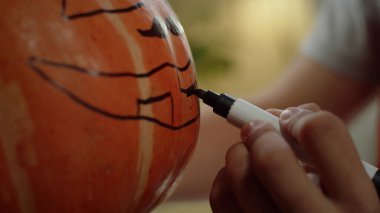 Genç bir adam balkabağının ağzını boyuyor.