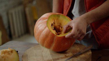 Genç bir adam balkabağının içini oyuyor ve onu çeviriyor.