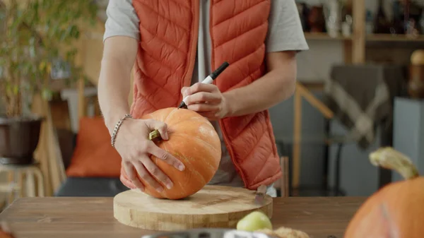 Un joven dibuja un patrón en una calabaza — Foto de Stock