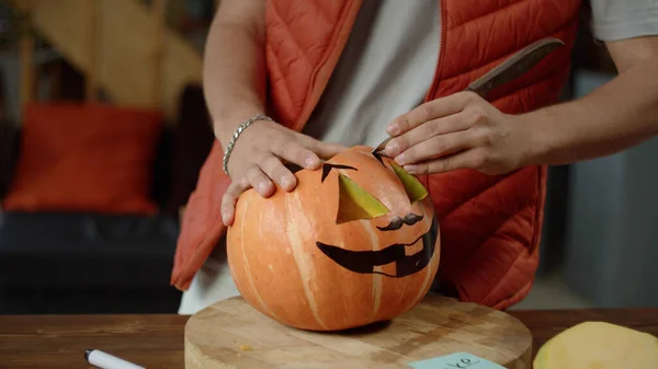 A young man in red vest carves brows of a halloween pumpkin Stock Picture