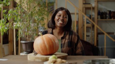 Güzel bir bayan balkabağıyla oturmuş kameraya bakıyor.