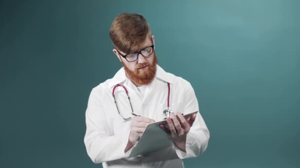 Jovem médico sorridente em óculos e com estatoscópio vestindo casaco branco em uma sala verde — Vídeo de Stock