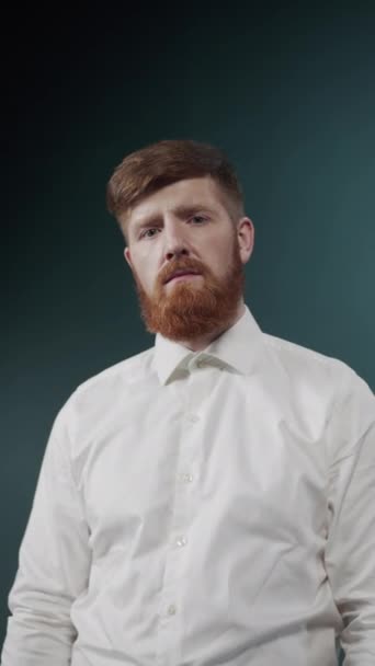Een jongeman met rood haar en baard toont een serieuze houding door zijn armen over de borst te kruisen — Stockvideo