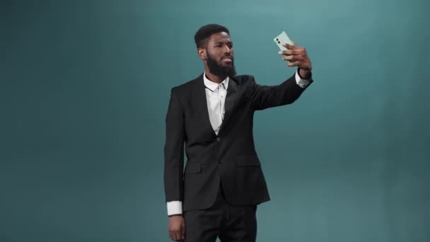 하얀 셔츠와 검은 수트를 입고 검은 수염을 한 잘생긴 아프리카 남자가 핸드폰으로 비디오를 만들고 있습니다. — 비디오