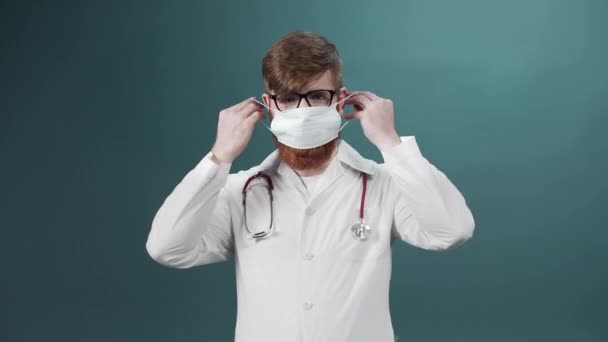 Hombre con barba con cara seria en bata de laboratorio pone máscara protectora sobre fondo de laboratorio verde — Vídeos de Stock