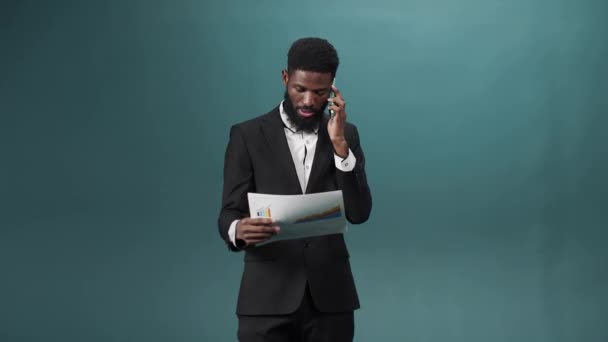 A man in a black tuxedo talks on the phone and has some questions about important documents — Stock Video