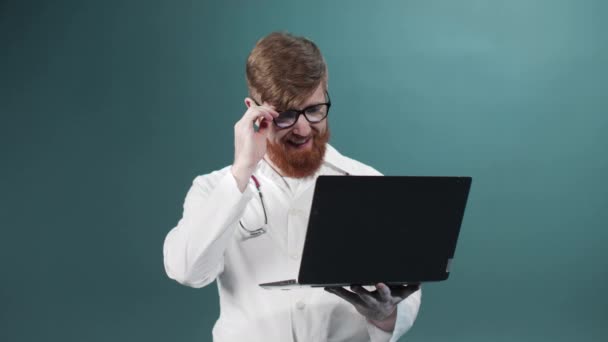 Ein junger rotbärtiger Arzt spricht mit seinem Freund im Internet und lächelt — Stockvideo