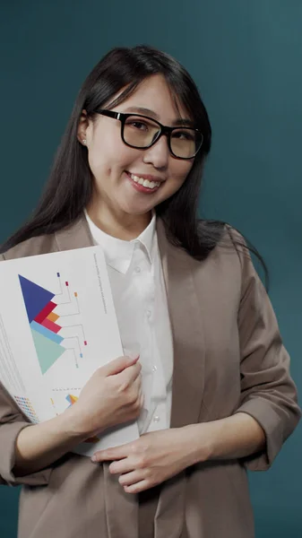 Ein Manager-Mädchen mit Brille, strenger Jacke und weißem Hemd, Laken in den Händen, auf denen Tabellen und Grafiken stehen. — Stockfoto