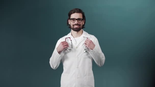Портрет уверенного молодого врача в очках и со статоскопом на зеленом фоне — стоковое видео