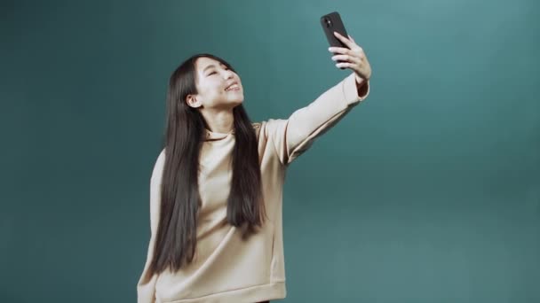 Chica bonita con el pelo largo y oscuro en sudadera con capucha beige hace selfie en su nuevo teléfono — Vídeos de Stock