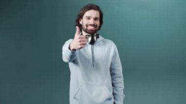 Tasasız, şık, beyaz tenli, kareli tişörtlü, başparmağı havada genç bir adam.