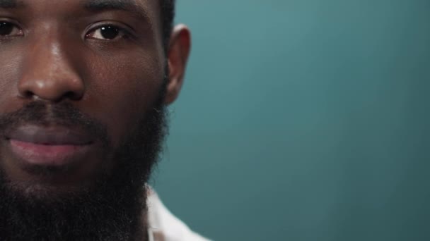 Een jonge zwarte man in een wit shirt kijkt serieus naar de camera. — Stockvideo