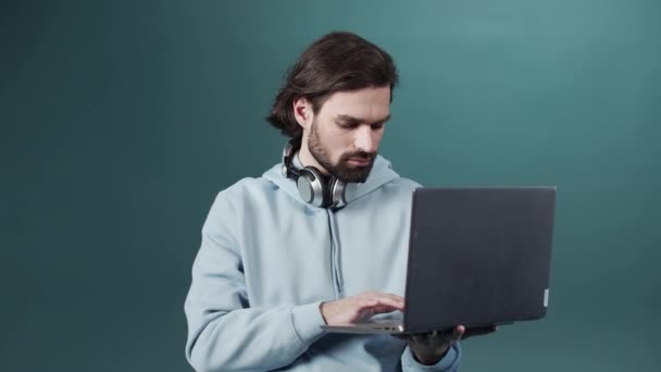 Ένα όμορφο λευκό δέρμα γενειοφόρος άνθρωπος στέκεται, κρατώντας ένα φορητό υπολογιστή στα χέρια του και την αναζήτηση μέσω του Διαδικτύου — Αρχείο Βίντεο