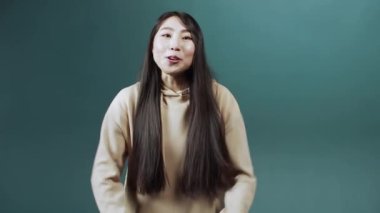 Uzun saçlı çekici bir Çinli kız kameraya konuşuyor, gülümsüyor ve el kol hareketi yapıyor.