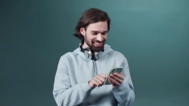 Gri kapüşonlu adam yeşil arka planda duruyor ve yeni akıllı telefondan video izliyor.