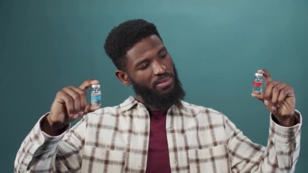 Um jovem negro atraente tenta comparar duas ampolas com a vacina. — Vídeo de Stock