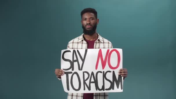 Un uomo nero attraente si leva in piedi e mostra un manifesto contro il razzismo — Video Stock