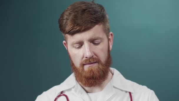 Человек с бородой с серьезным лицом в лабораторном халате надевает защитную маску на зеленый фон лаборатории — стоковое видео