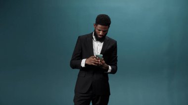 Beyaz gömlekli, siyah takım elbiseli, siyah sakallı yakışıklı bir Afrikalı telefonunda video çekiyor.