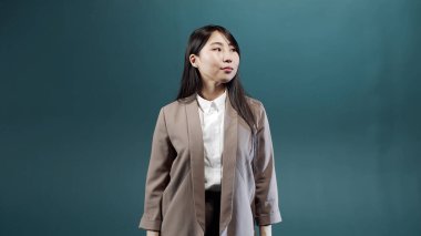 Bej ceketli ve beyaz bluzlu ciddi bir kız kollarını kavuşturup kameraya bakıyor.