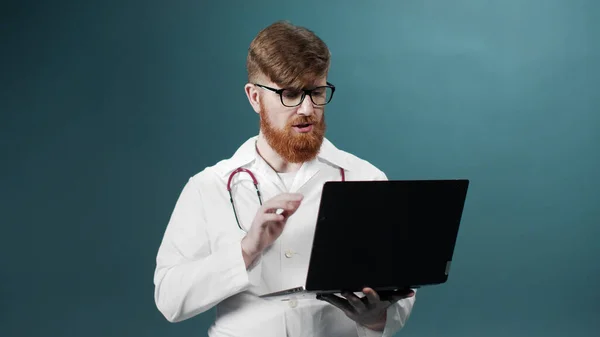 A young red bearded doctor is taking a video consultation on the Internet with his patient — Stock Photo, Image