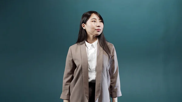 Bej ceketli ve beyaz bluzlu ciddi bir kız kollarını kavuşturup kameraya bakıyor.