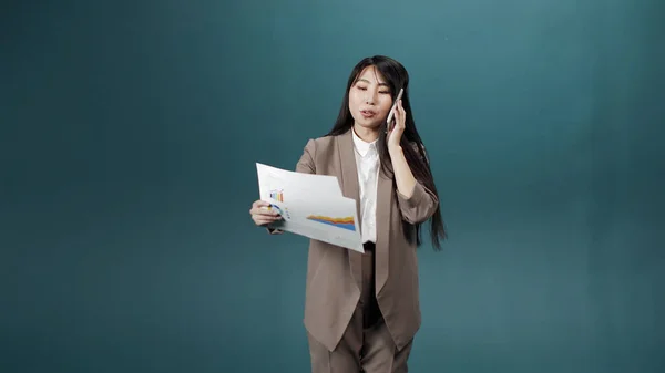 A manager girl in a beige jacket and a white shirt with papers in her hands talking to the phone Royalty Free Stock Photos