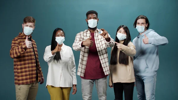 En interracial gruppe viser en ampul med vaccine mod coronavirus og gør en tommelfinger-up tegn Stock-foto