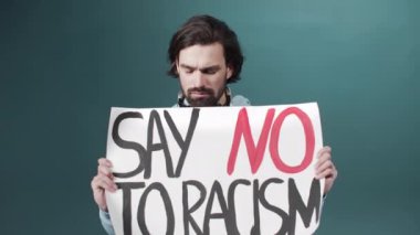 Mavi kapüşonlu yetişkin bir beyaz adam ağır çekimde ırkçılığa karşı bir poster asıyor.