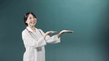 Siyah saçlı bir Asyalı doktor poz veriyor, başparmağıyla kameraya bakıyor.