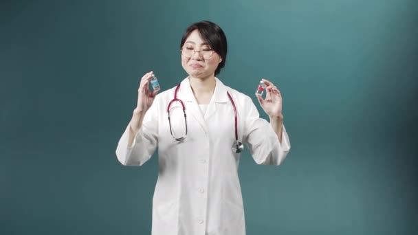 Egy vonzó fiatal orvos mosolyog, és két ampullát mutat be a koronavírus elleni vakcinával, és kiválaszt egy jobbat. — Stock videók