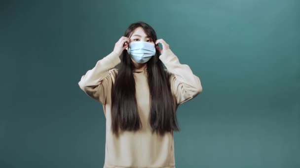 En söt asiatisk flicka lägger av ansiktet en skyddande mask och ler — Stockvideo