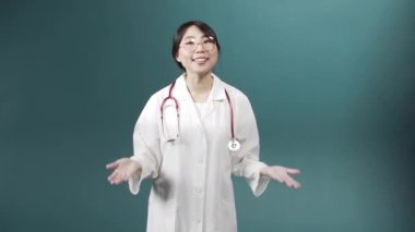 Beyaz tıp önlüklü çekici bir doktor kameraya konuşuyor, gülümsüyor ve işaret ediyor.